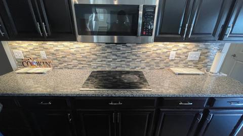 Dark kitchen cabinetry, stone countertop and tile backsplash