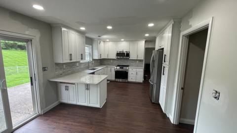 After: remodeled kitchen with white cabinetry, a peninsula and wood-look flooring